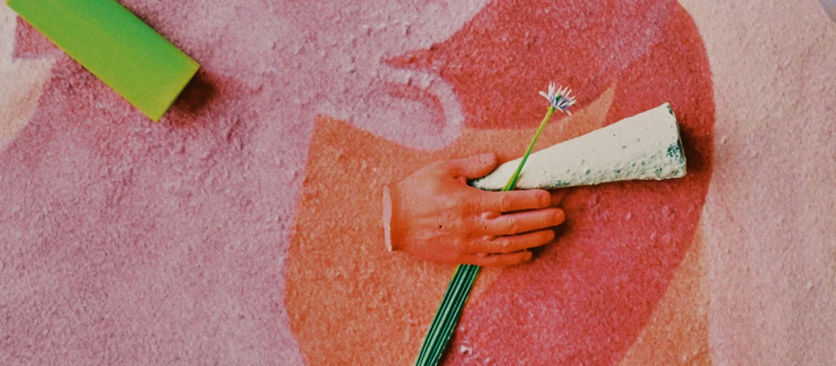 A closeup of an abstract painting on a flat surface. On top the is an object that resembles a cannabis joint held by a tiny clay hand. at the edge of the picture is a BIC lighter.